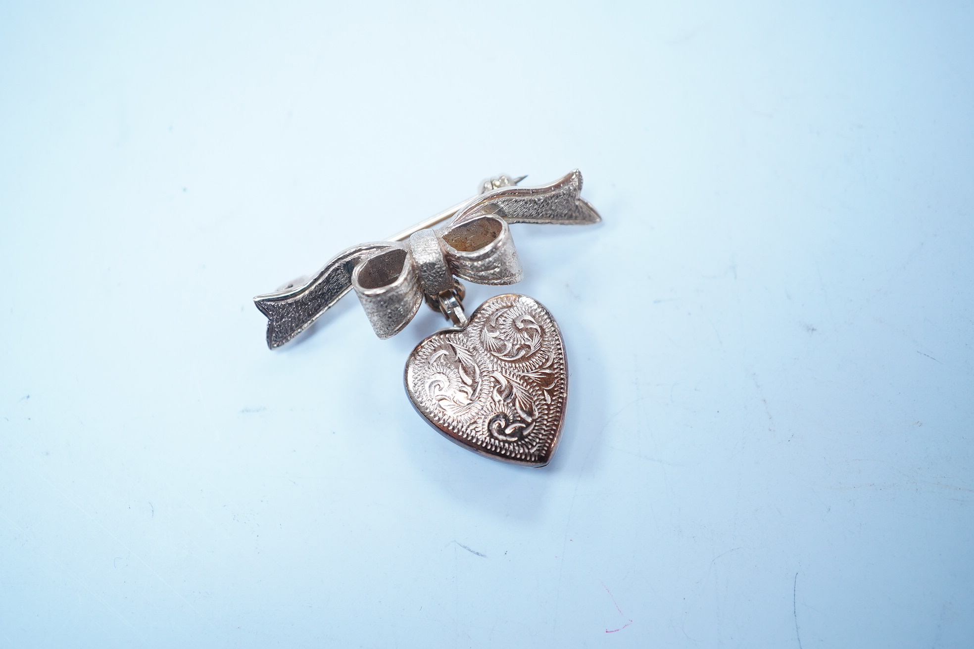 A modern engraved 9ct gold heart shaped locket, on an associated 9ct gold ribbon bow suspension brooch, width 31mm, gross weight 4.2 grams. Condition - fair to good